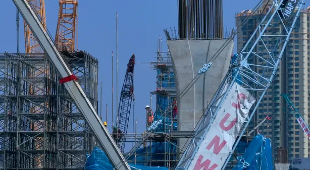 Cranes lifting steelwork beside a completed concrete pier on the RTS Link alignment