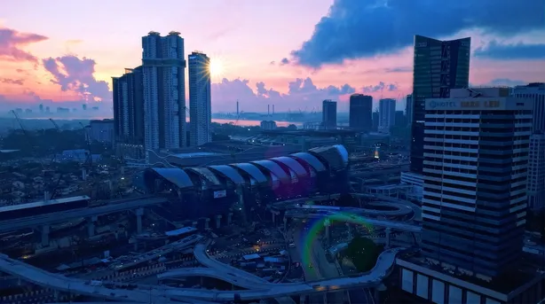 Bukit Chagar station and the Johor Bahru skyline from the air at dusk, the station roof lit against the city