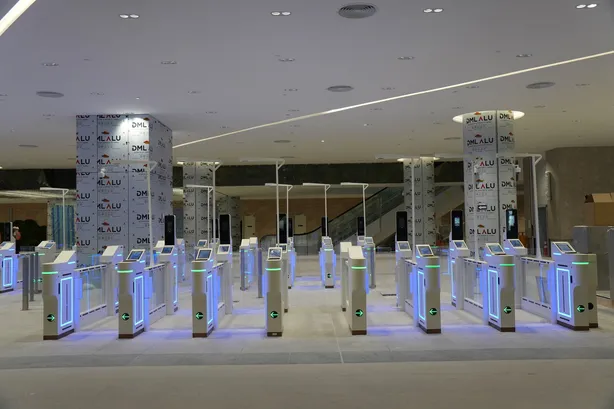The Malaysia immigration hall at the ICQ Complex, banks of autogates lit blue and green with their lane arrows showing