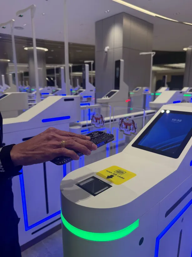 A traveller holding a phone over the QR reader on an autogate, the gate ring lit green beneath it
