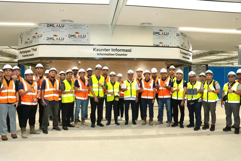 The MCMC delegation and RTS Link site teams in hard hats and high-visibility vests, gathered in front of the ICQ Complex information counter