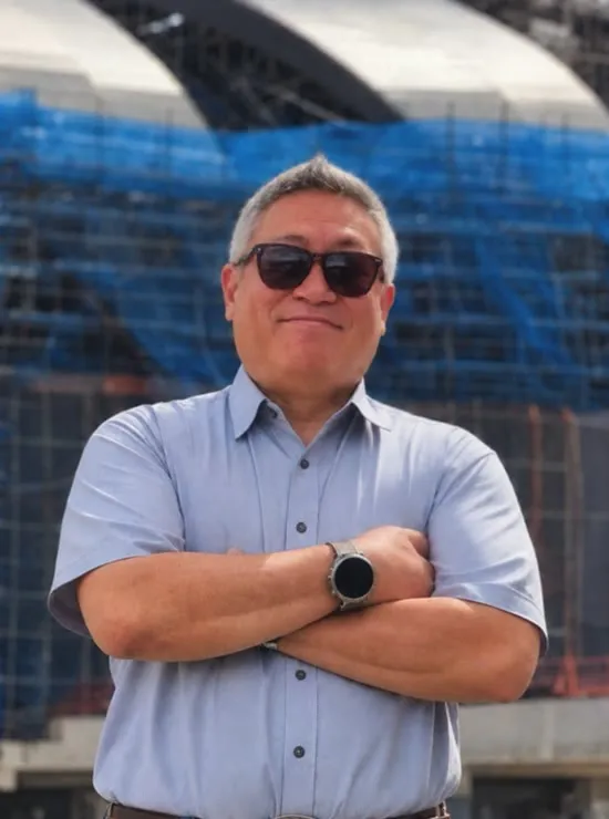 Nasharuddin Zaini in an MRTS shirt and sunglasses, arms crossed on a site road in front of a station under construction with a crane in the background