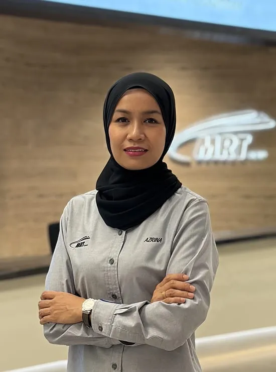 A woman in a headscarf and MRT corporate attire standing with arms crossed in front of the RTS Link information counter