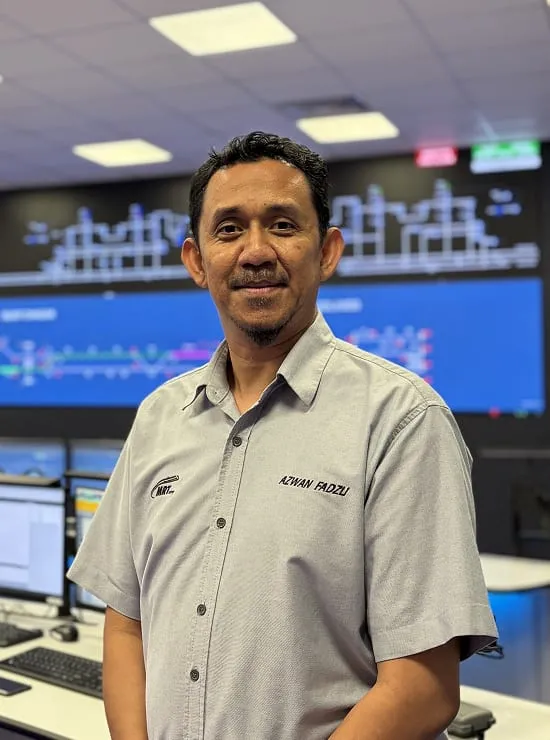 A man standing in the operations control room with railway system displays lit up on the screens behind him
